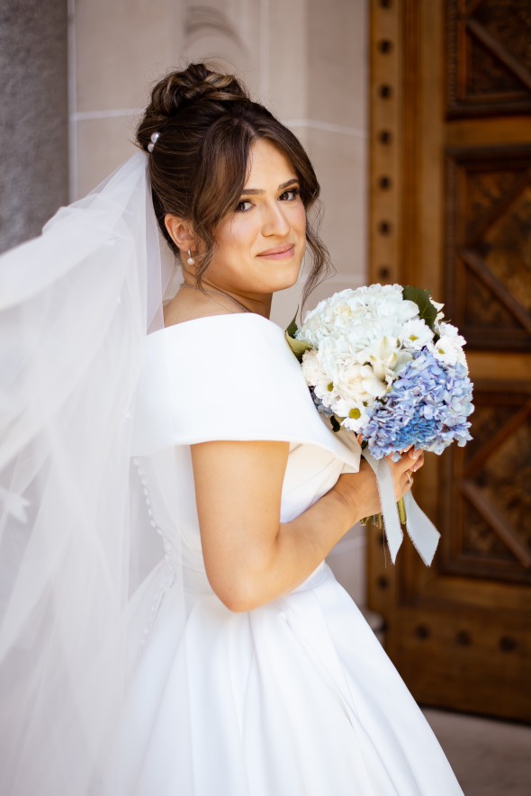 Bride at carved doors with blue and white hydrangea bouquet
