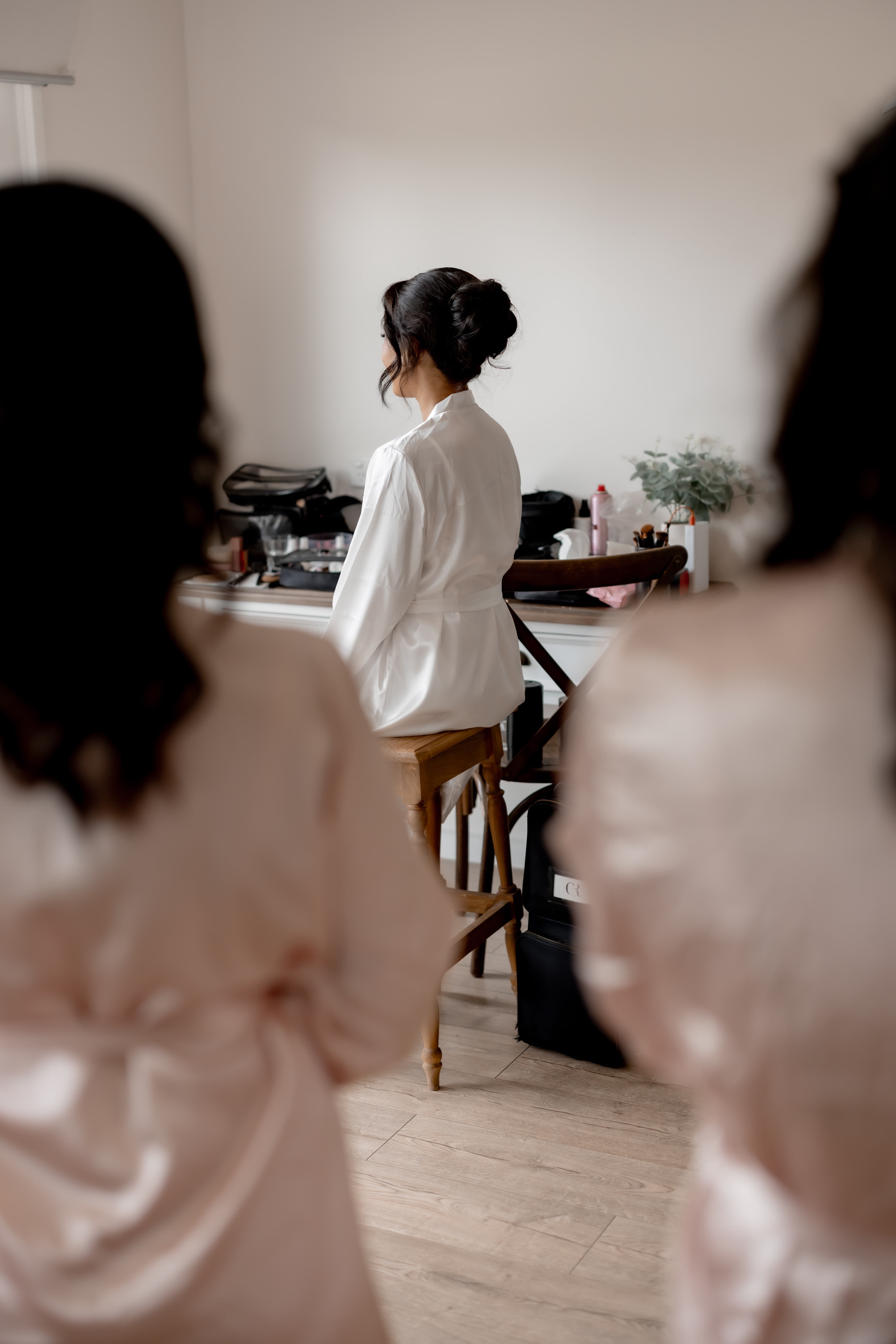 Bride in white robe getting ready while bridesmaids look on — Marikate Makeup Melbourne
