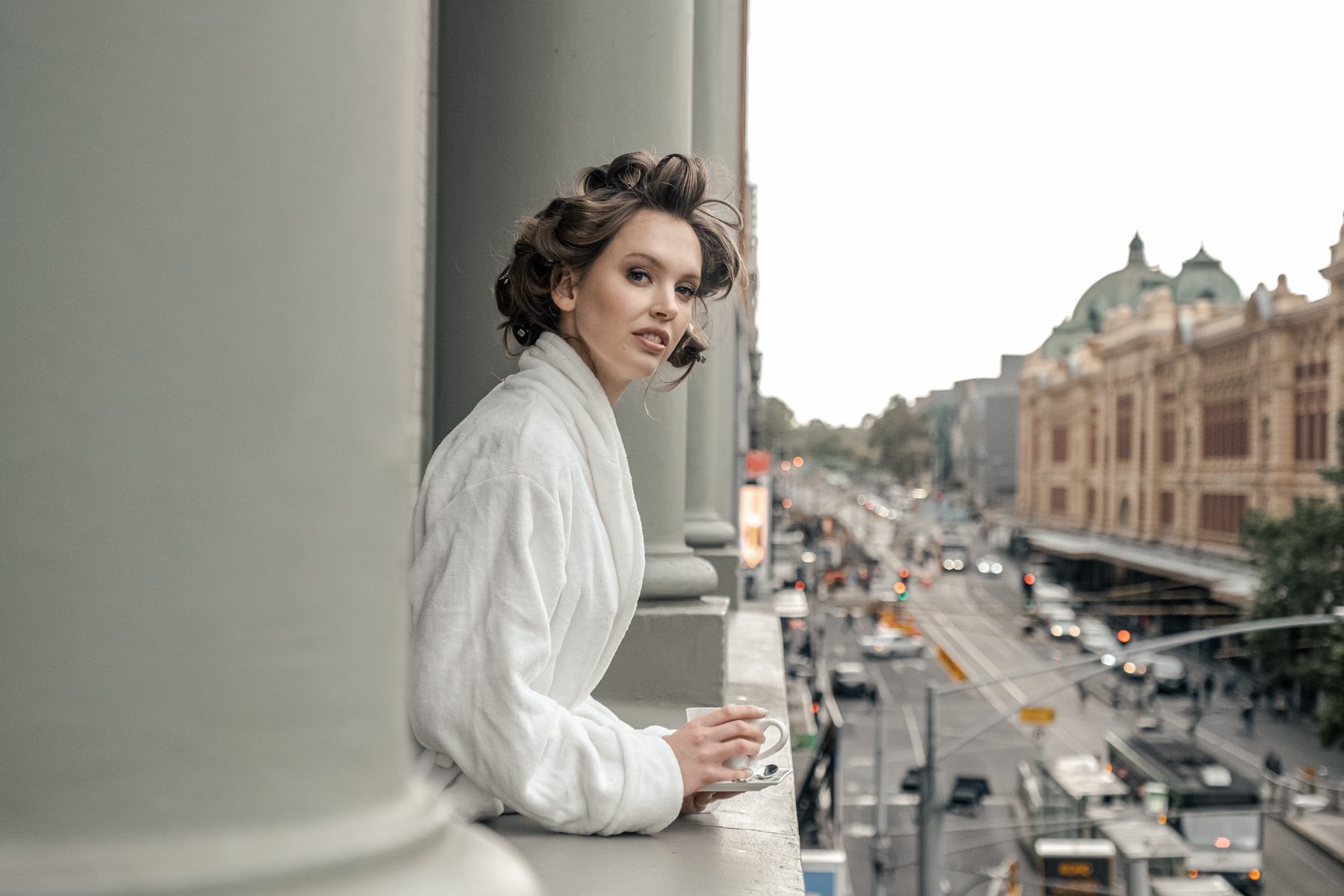 Bride in a robe with hair in rollers, looking out over Melbourne from a balcony — Marikate Makeup